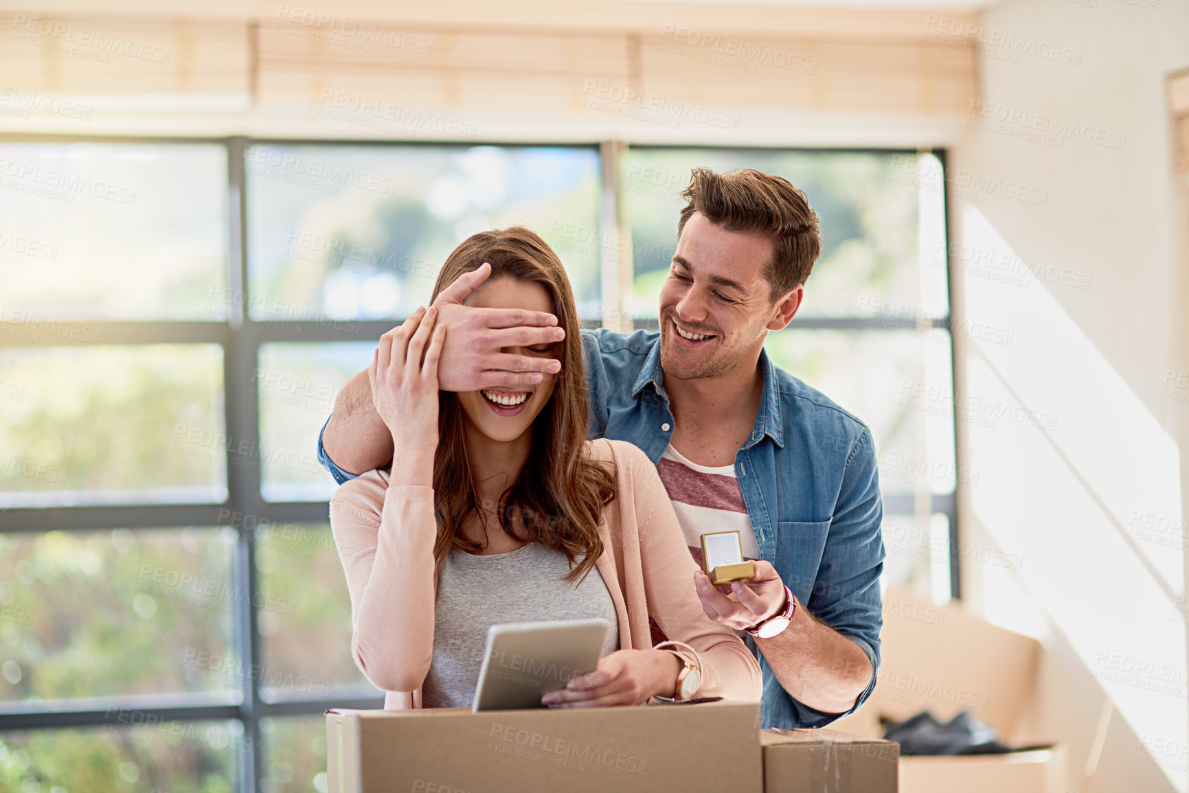Buy stock photo Couple, home and moving with propose surprise, man and hand for closed eyes gesture or woman browsing on tablet. New opportunity, partner and engagement box for marriage, living room and apartment