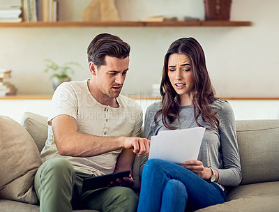 Buy stock photo Shot of a young couple going through their paperwork together at home and looking worried