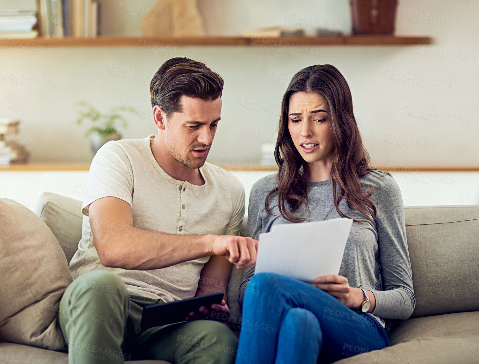 Buy stock photo Shot of a young couple going through their paperwork together at home and looking worried