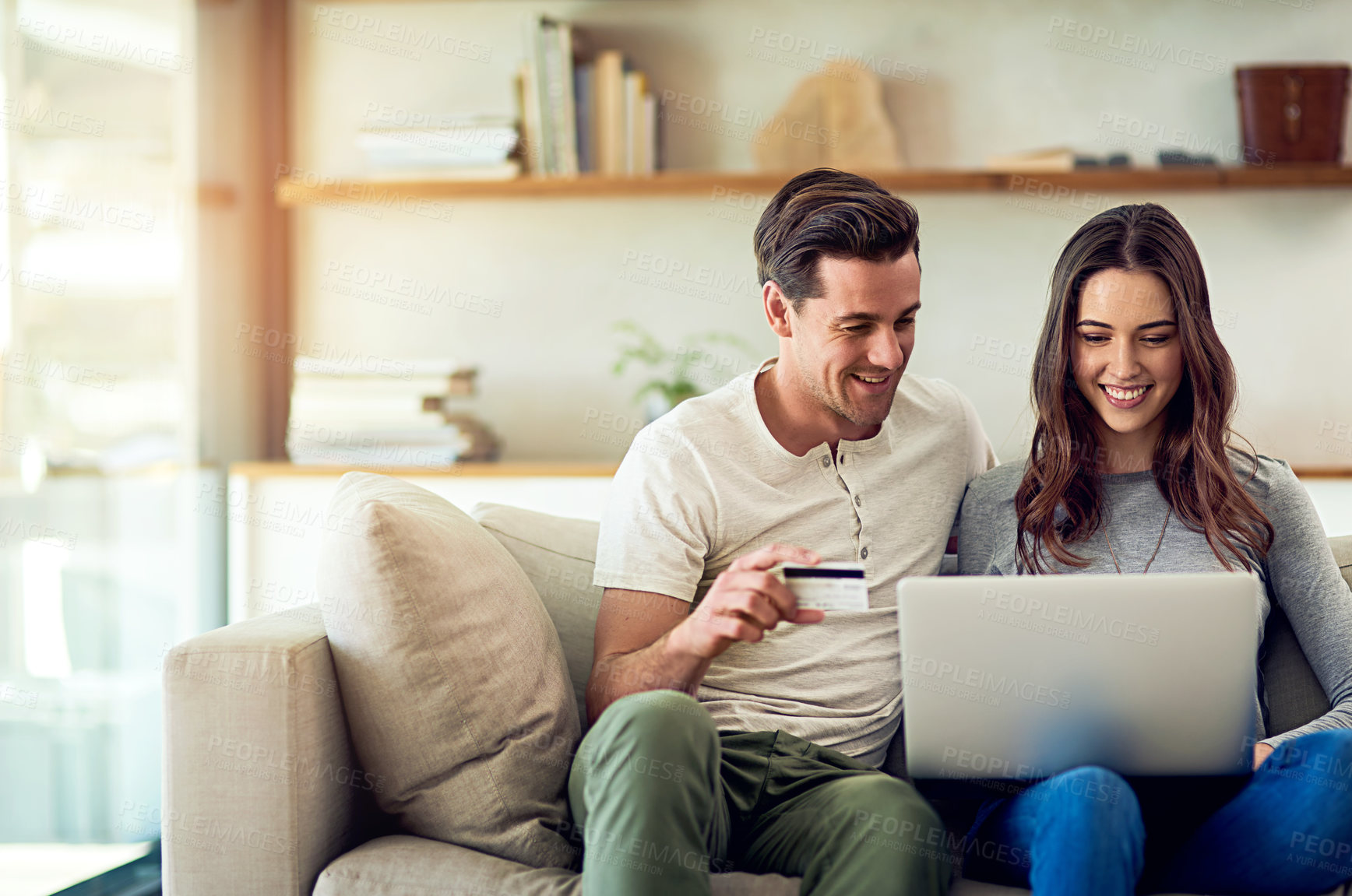 Buy stock photo Shot of a happy young couple making a credit card payment on a laptop together at home