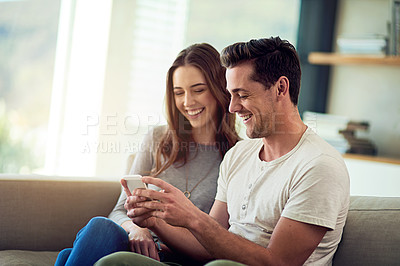 Buy stock photo Shot of a happy young couple using a phone together on the sofa at home