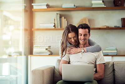 Buy stock photo Shot of a young woman hugging her husband while he uses a laptop on the sofa at home