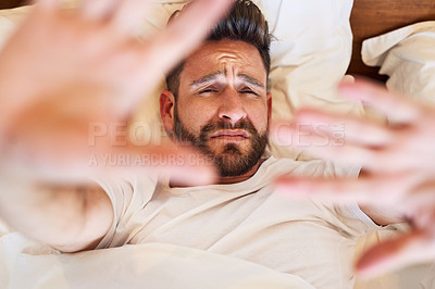 Buy stock photo High angle shot of a young man shielding his face while waking up from bed
