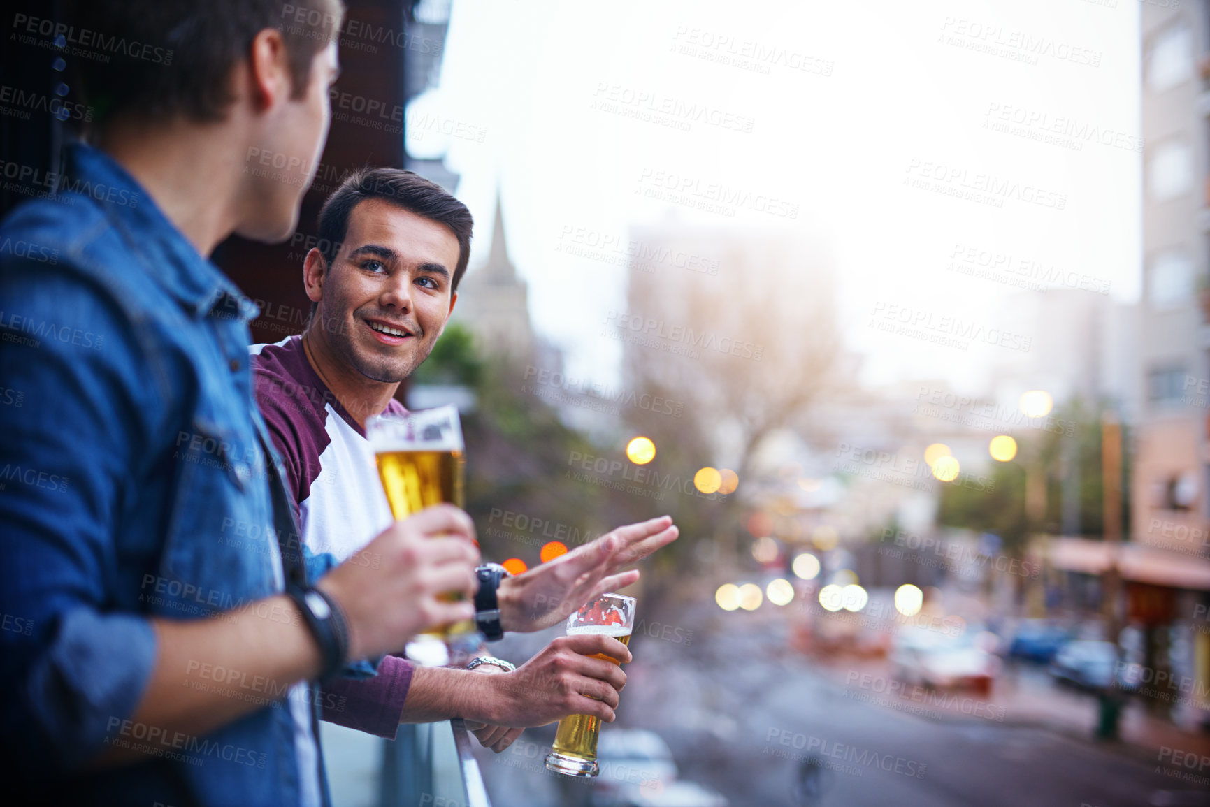 Buy stock photo Cropped shot of two guys drinking beer while standing on the balcony at a party