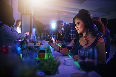 Buy stock photo Cropped shot of a young woman texting on her cellphone while standing in a nightclub
