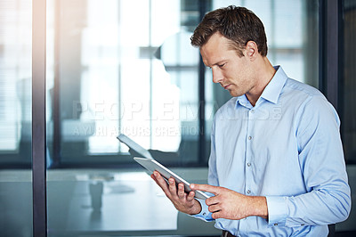 Buy stock photo Shot of a well dressed businessman using a tablet while standing in the office