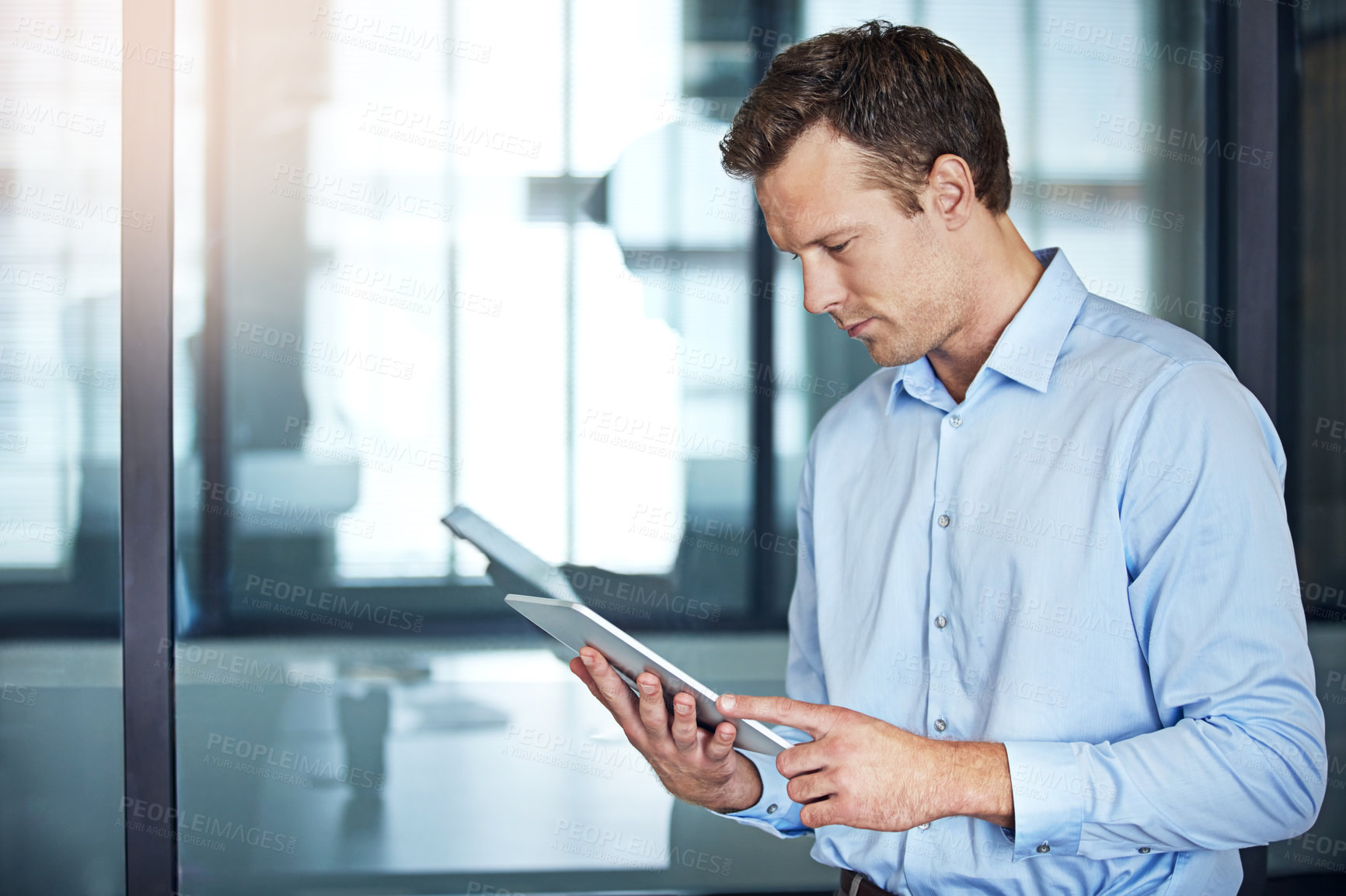 Buy stock photo Shot of a well dressed businessman using a tablet while standing in the office