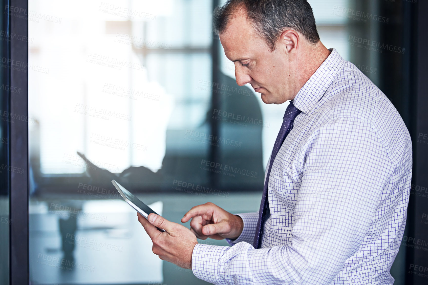 Buy stock photo Shot of a well dressed businessman using a tablet while standing in the office