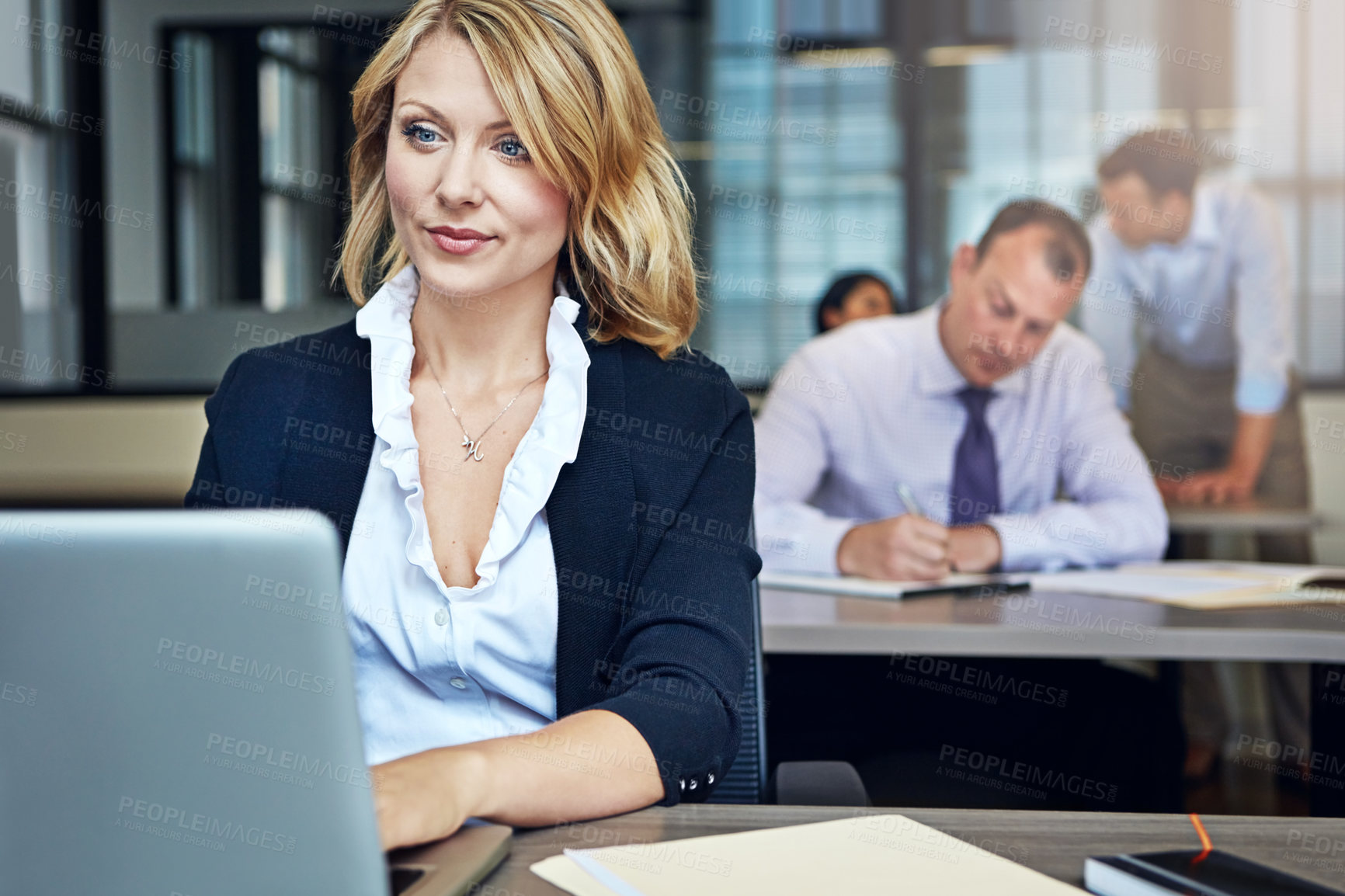 Buy stock photo Shot of a businesswoman using a laptop at her desk with her colleagues in the background