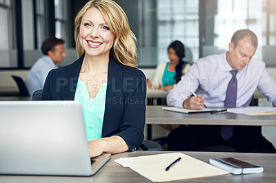 Buy stock photo Portrait of a businesswoman using a laptop at her desk with her colleagues in the background