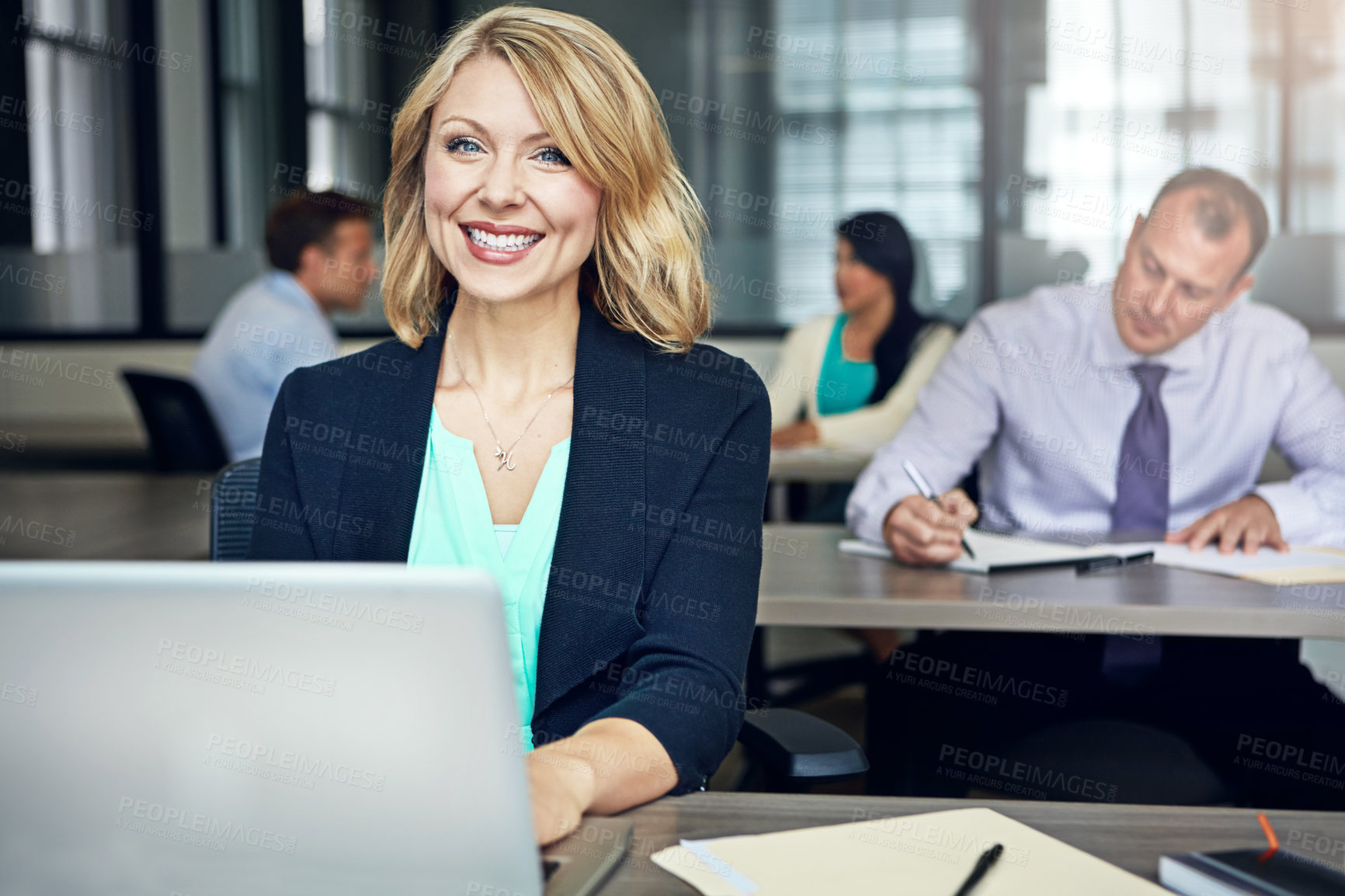 Buy stock photo Portrait of a businesswoman using a laptop at her desk with her colleagues in the background