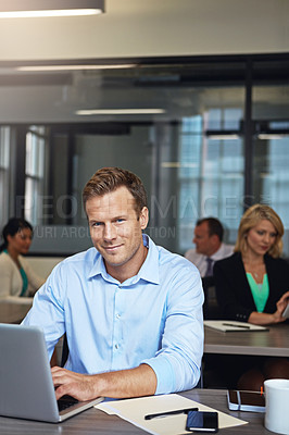 Buy stock photo Portrait of a businessman using a laptop at his desk with his colleagues in the background