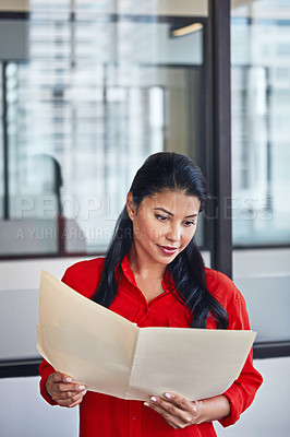 Buy stock photo Shot of a casually dressed businesswoman reading through paperwork in the office