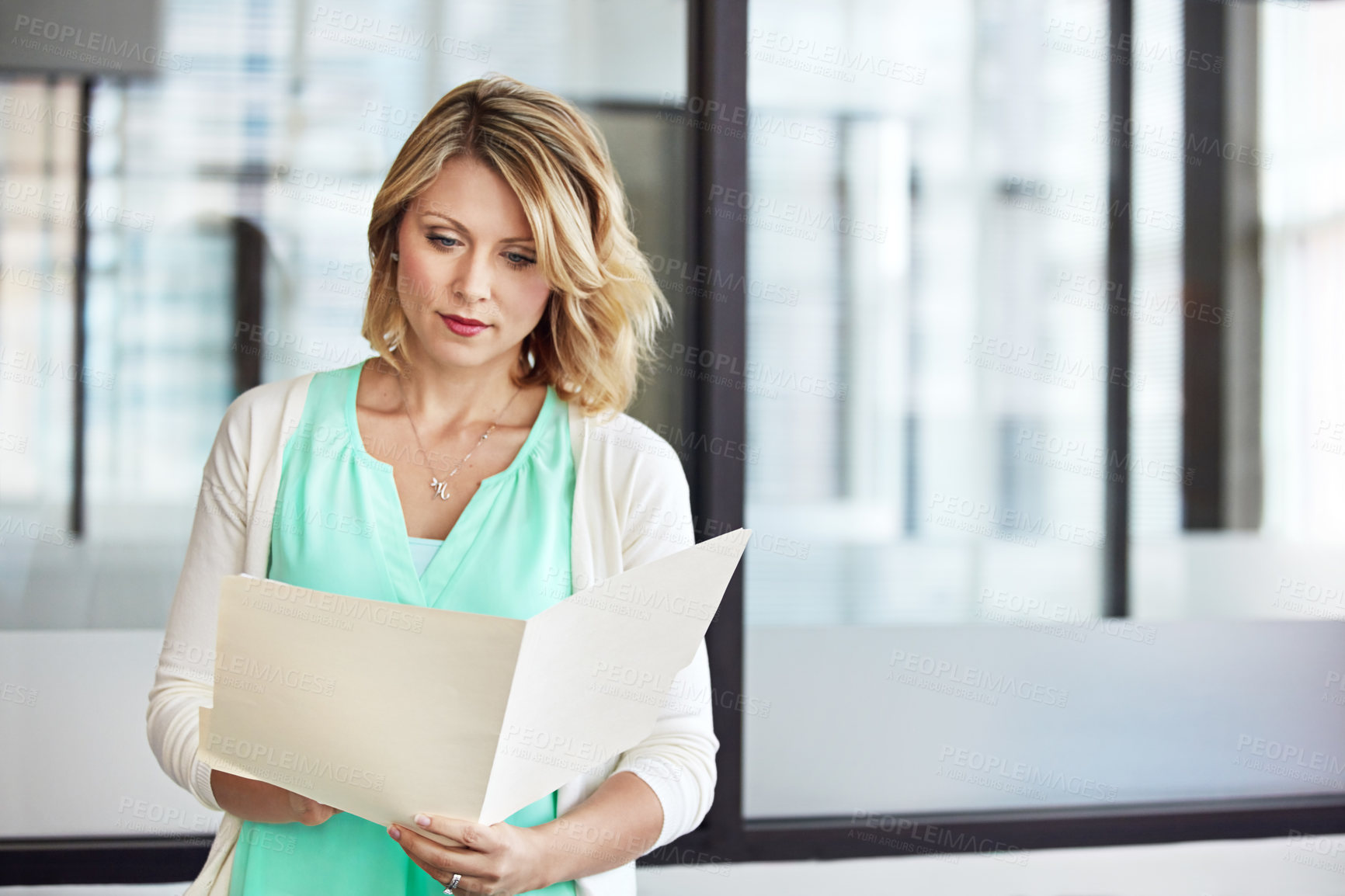 Buy stock photo Shot of a casually dressed businesswoman reading through paperwork in the office