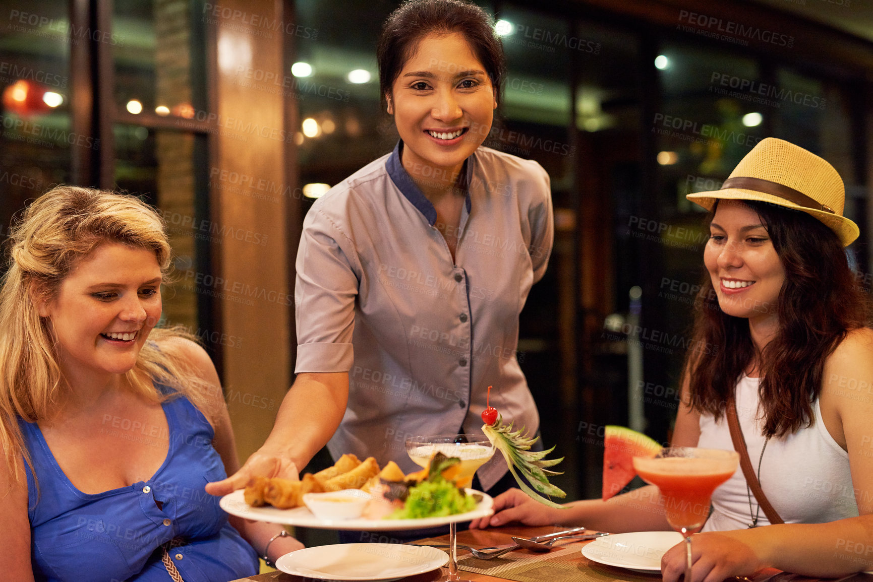 Buy stock photo Waiter, portrait and food at restaurant for customers, dinner and women eating together with service. Employee, smile and hospitality with cocktails or platter in diner at night for celebration