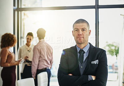 Buy stock photo Portrait of a businessman standing with his arms folded while some colleagues talk in the background