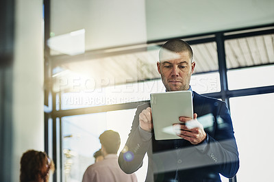 Buy stock photo Shot of a businessman using his tablet while some colleagues talk in the background