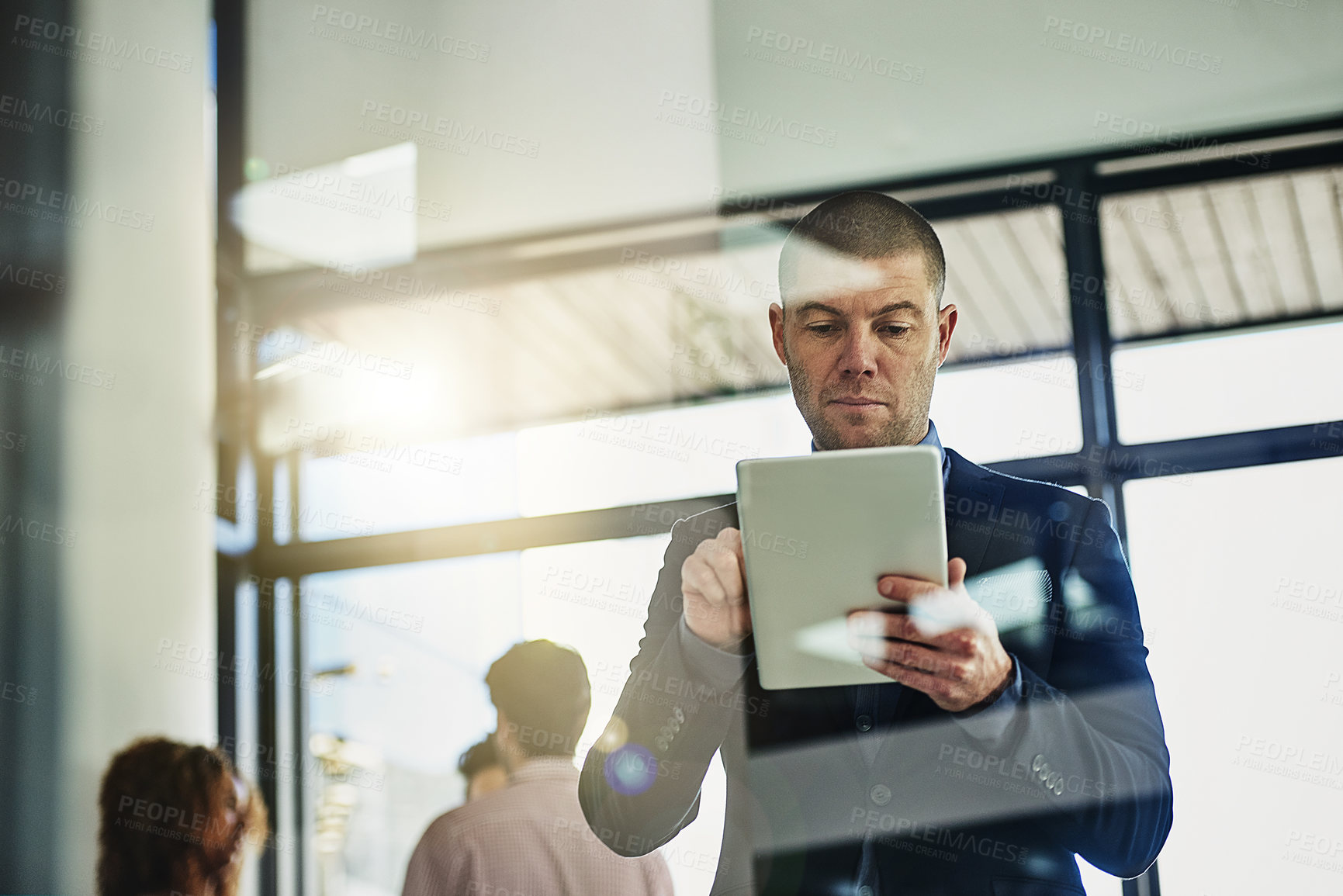 Buy stock photo Shot of a businessman using his tablet while some colleagues talk in the background