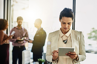 Buy stock photo Shot of a businesswoman using her tablet while some colleagues talk in the background