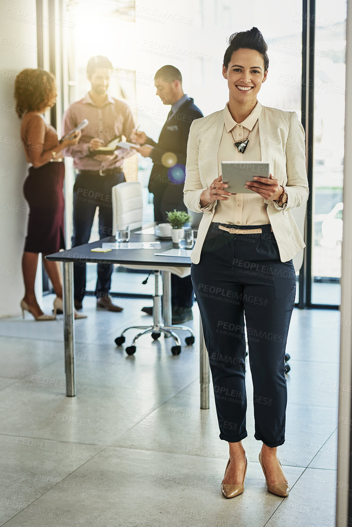 Buy stock photo Portrait of a businesswoman using her tablet while some colleagues talk in the background