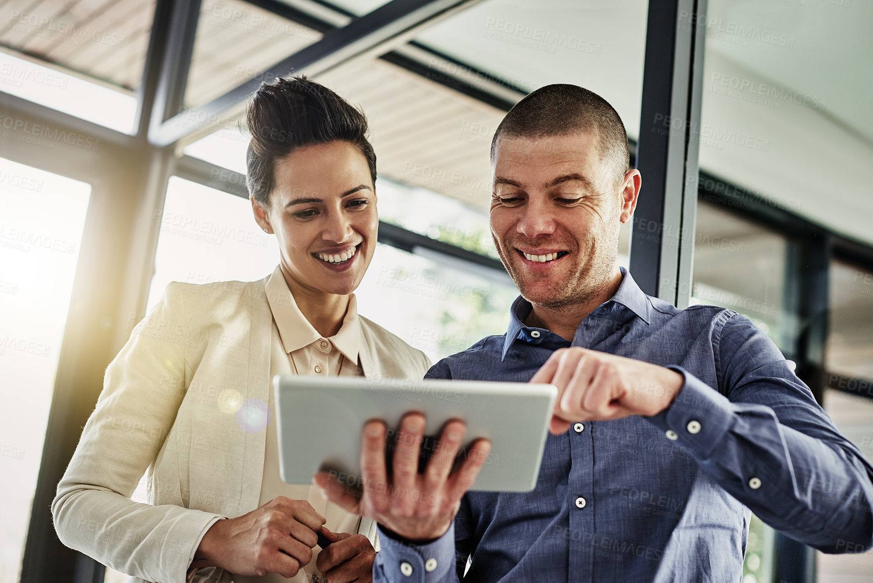 Buy stock photo Shot of two colleagues using a tablet while meeting in their office