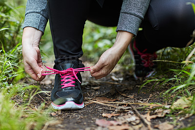 Buy stock photo Shot of an unidentifiable young woman tying her shoelaces while hiking in the forest