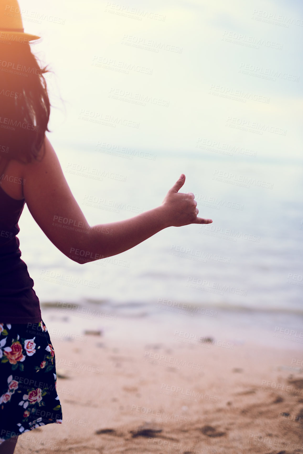 Buy stock photo Rearview shot of a young woman at the beach gesturing hang ten