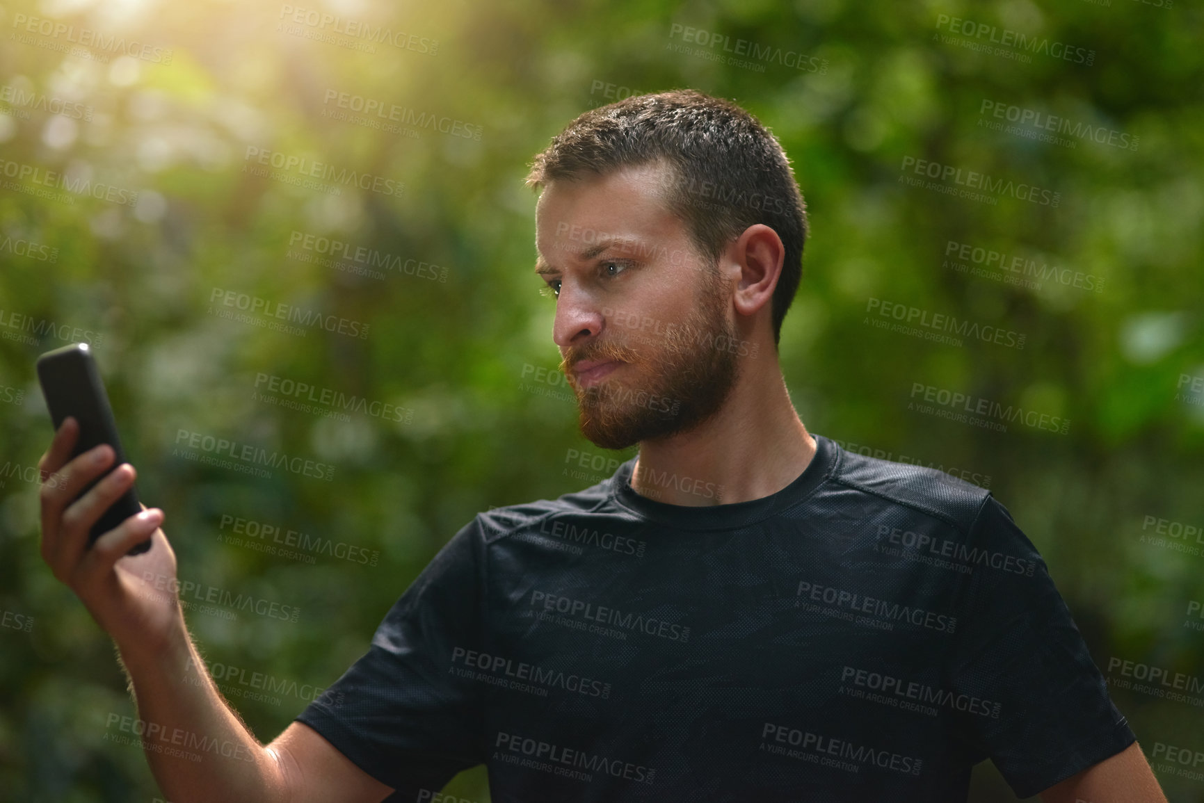 Buy stock photo Shot of a young man using his cellphone while standing alone in a jungle