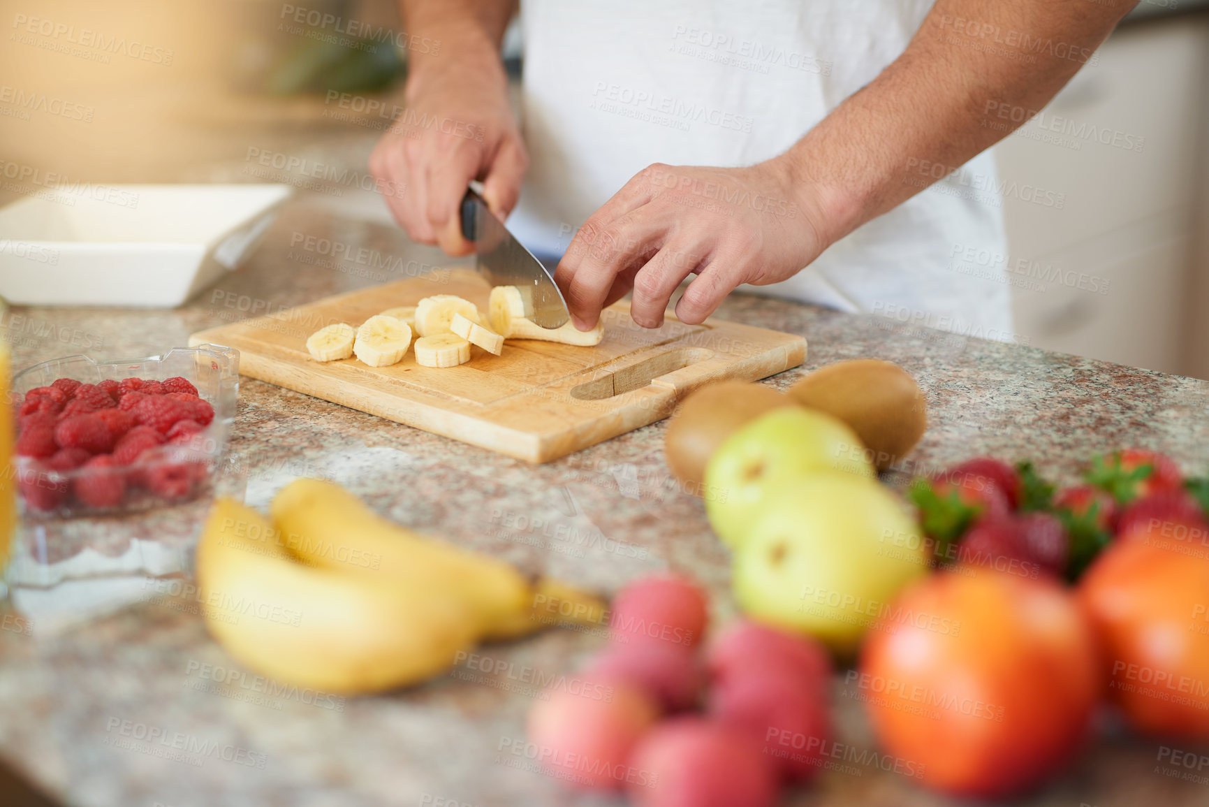 Buy stock photo Cropped shot of a young man making a fruit salad in his kitchen