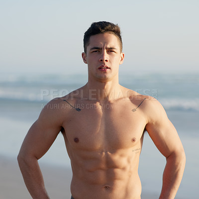 Buy stock photo Cropped portrait of a handsome young man standing with his hands on his hips at the beach