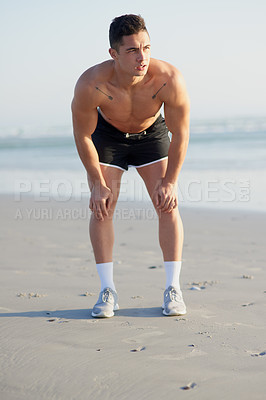 Buy stock photo Full length shot of a handsome young man looking tired after a run on the beach