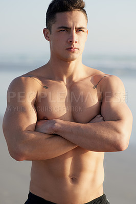 Buy stock photo Cropped shot of a handsome young man standing with his arms folded at the beach