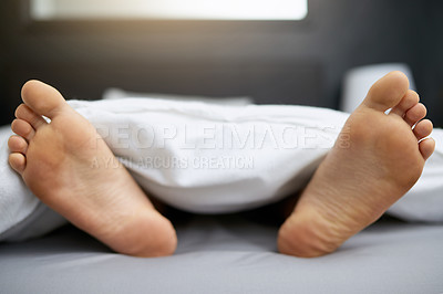 Buy stock photo Shot of a young man's feet sticking out from underneath his duvet