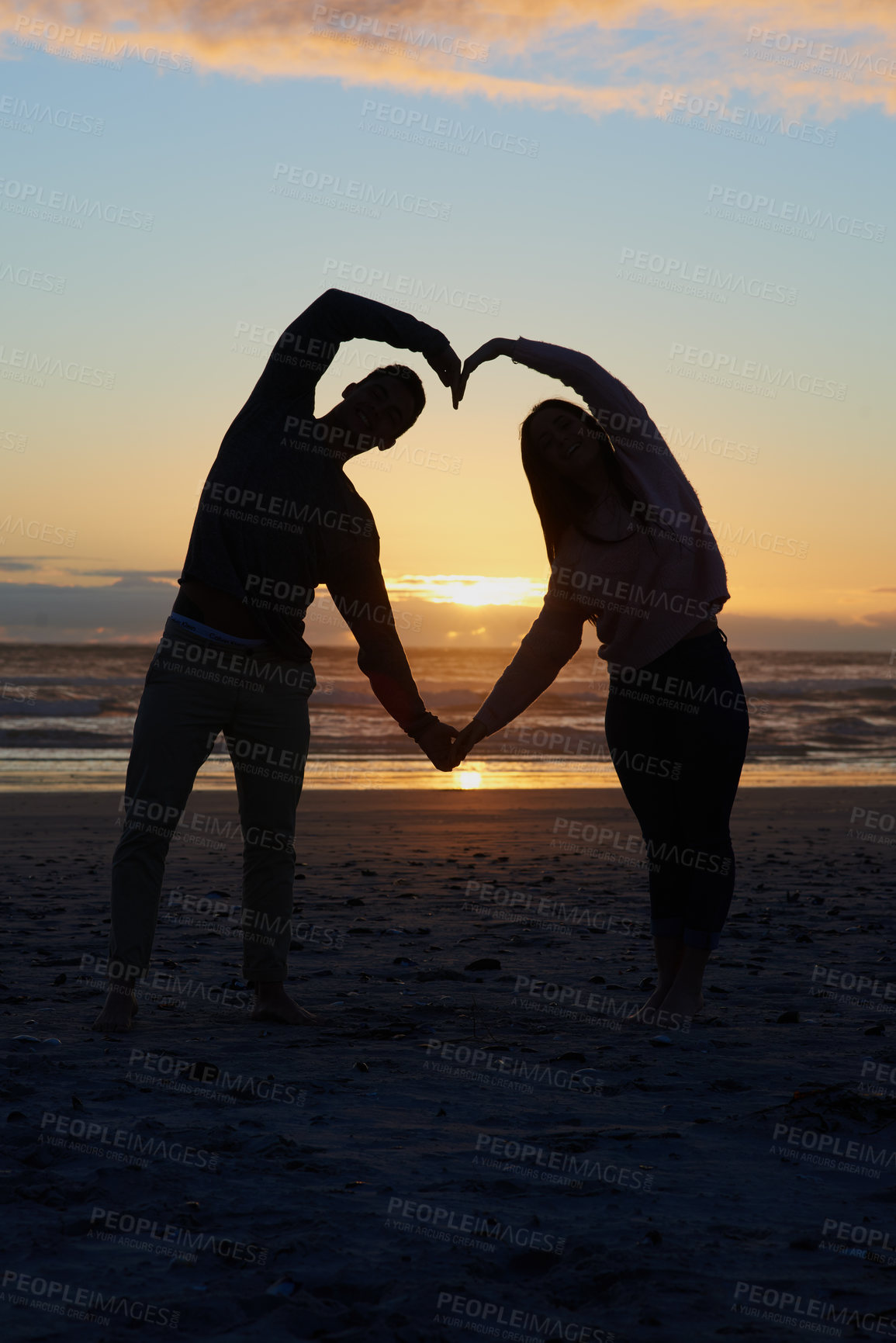 Buy stock photo Silhouette shot of a young couple on the beach