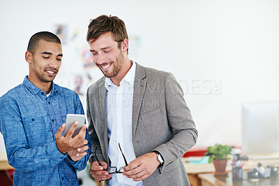 Buy stock photo Shot of two coworkers having a discussion while looking at a cellphone
