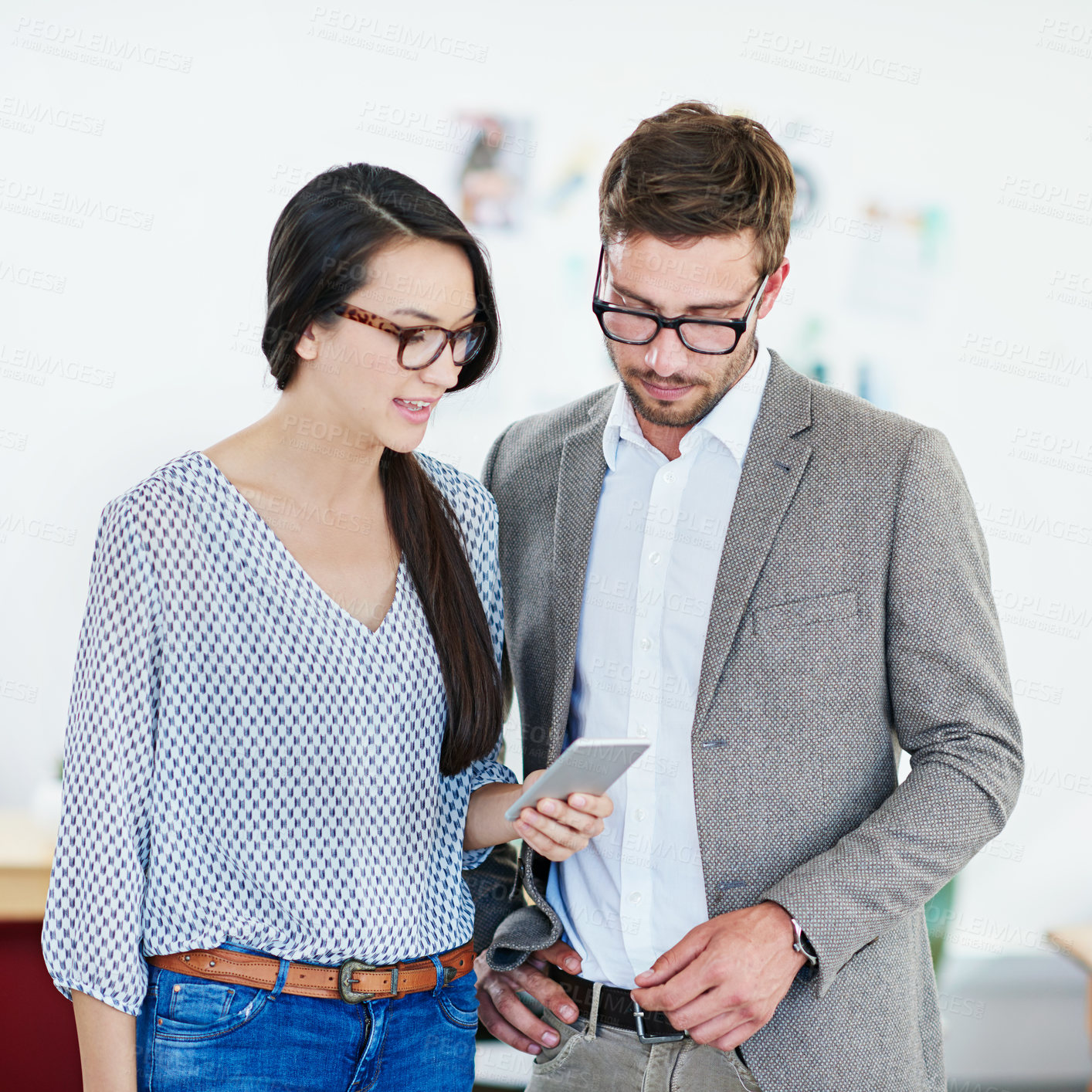 Buy stock photo Shot of two coworkers having a discussion while looking at a cellphone