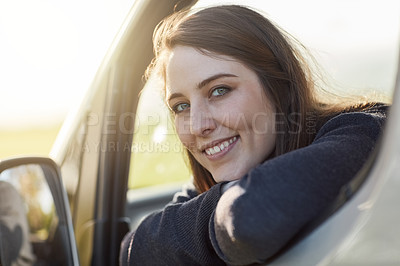 Buy stock photo Portrait of a happy young woman looking out of the window of her car while out on a roadtrip