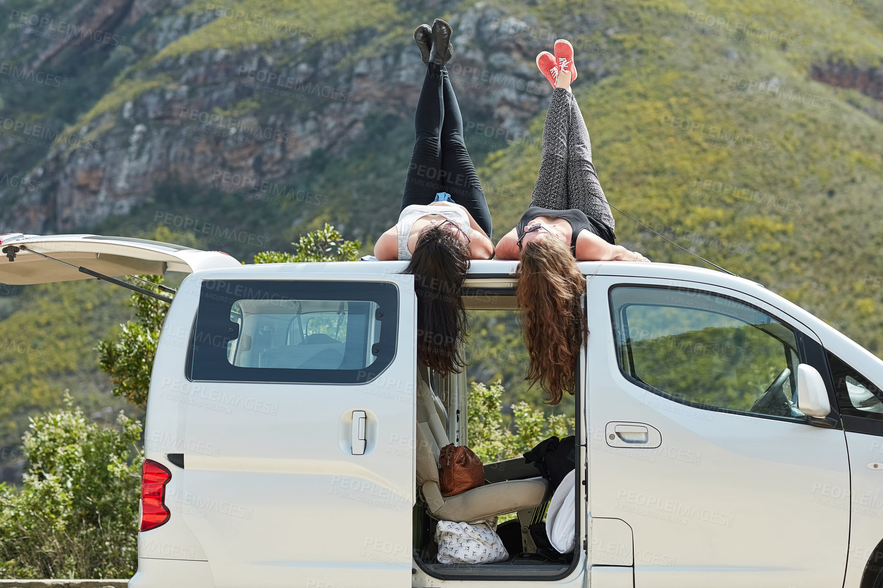 Buy stock photo Shot of two young friends lying on the roof of their car while out on a roadtrip