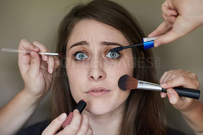 Buy stock photo Concept shot of a nervous looking young woman with an assortment of brushes applying makeup to her face
