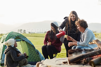 Buy stock photo Shot of a group of young friends enjoying coffee by the fire while on a camping trip