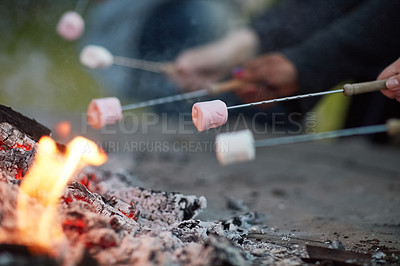 Buy stock photo Shot of a group of unidentifiable friends roasting marshmallows by a campfire