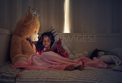 Buy stock photo Shot of a little girl using a digital tablet while lying in bed with her teddy at night