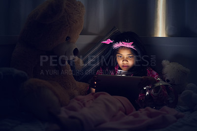 Buy stock photo Cropped shot of a little girl using a digital tablet while lying in bed with her teddy at night