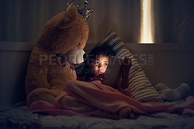 Buy stock photo Shot of a little girl using a digital tablet while lying in bed with her teddy at night
