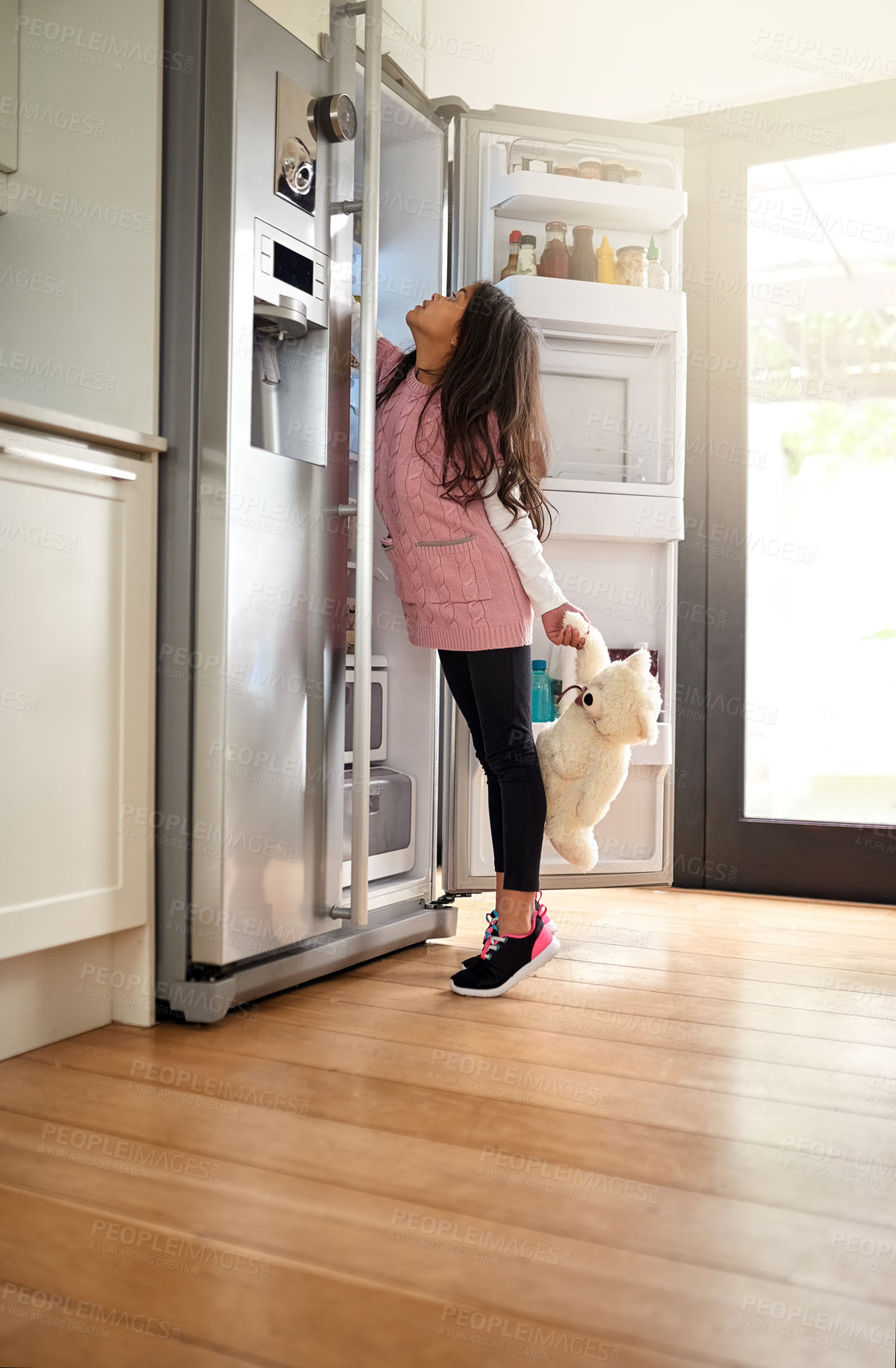 Buy stock photo Shot of a little girl reaching for something in the fridge at home