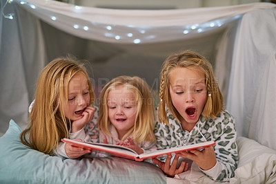 Buy stock photo Shot of three little sisters reading a book together before bedtime