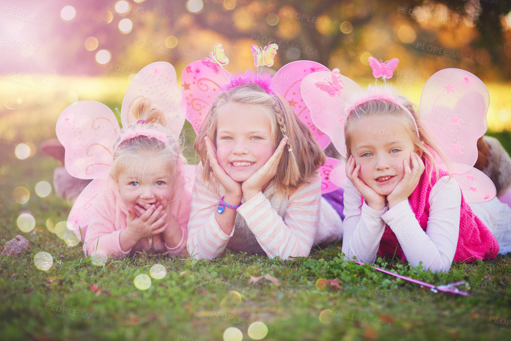 Buy stock photo Outdoor, fairy and portrait of sisters lying in field with wings for dress up, princess outfit or cosplay. Bokeh, nature and young children with smile for fantasy play, childhood or halloween costume