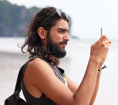 Buy stock photo Shot of a young man taking pictures on his phone at the coast