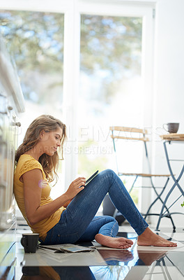 Buy stock photo Shot of an attractive young woman chilling on her kitchen floor using a digital tablet
