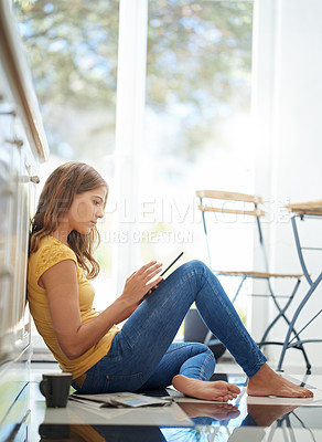Buy stock photo Shot of an attractive young woman chilling on her kitchen floor using a digital tablet